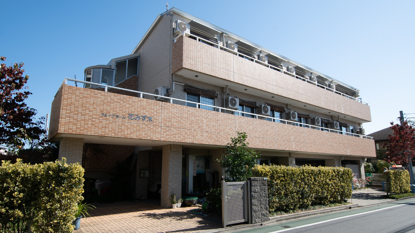 レンガ造りの介護施設の建物外観。複数階建てで、前庭には植栽が配置されている。